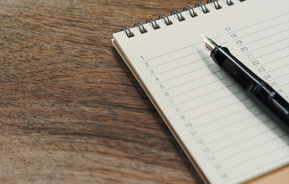 A fountain pen resting on a paper reading list on a wooden table.png