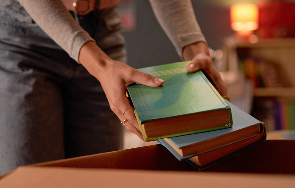 Woman putting two books into a box to sell them.png