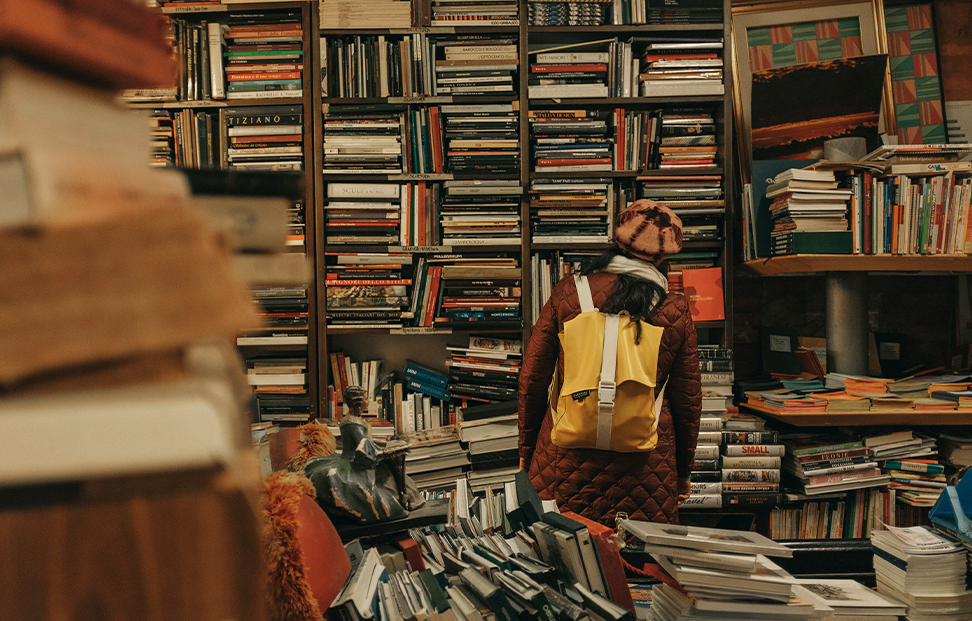 Woman with a yellow rucksack looking at books in a bookshop.png