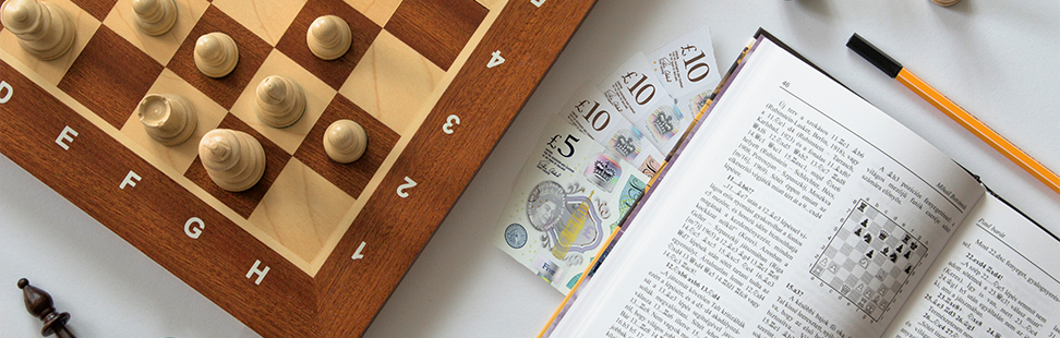 wooden chessboard next to cash and a chess book header image.png